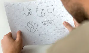 Szkice symboli i wzorów, w tym potencjalny sigil, na papierze w kropki.