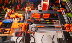 Drukarka 3D z pomarańczowymi elementami i szpulą filamentu. Optymalna temperatura dla PETG jest kluczowa dla udanych wydruków.