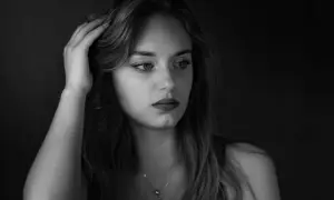 Portret młodej kobiety w odcieniach **black color**. Jej dłoń spoczywa na włosach, a wzrok skierowany jest w bok, w głąb mroku.