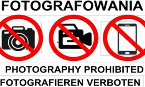 Tablica informuje o zakazie fotografowania. Widoczne są symbole aparatu, kamery i telefonu komórkowego przekreślone czerwoną linią.