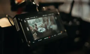 Ekran monitora kamery filmowej pokazuje scenę z kobietą czytającą książkę przy stoliku. To ujęcie z planu filmowego.