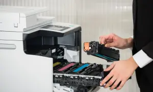 Osoba w czarnym garniturze wymienia toner w drukarce laserowej. Czy drukarka laserowa ma tusz? Nie, używa proszku.