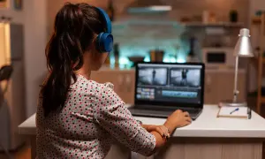 Kobieta w słuchawkach pracuje na laptopie, edytując film. Uczy się, jak zmniejszyć rozmiar filmu, by był łatwiejszy do udostępnienia.