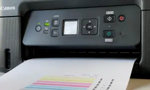 Drukarka Canon wyświetla komunikat "Do którego deseniu jest najbardziej podobny Twój zadrukowany?". Papier z kolorowymi paskami jest częściowo wysunięty.
