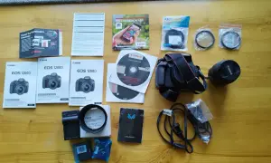 Zestaw akcesoriów do aparatu Canon EOS 1200D: aparat, obiektyw, ładowarka, filtry, instrukcje i płyty DVD.