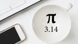 Biała filiżanka z symbolem pi i liczbą 3.14, obok smartfon i fragment laptopa.