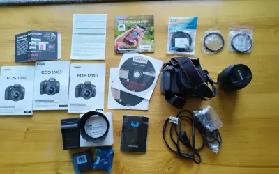 Zestaw akcesoriów do aparatu Canon EOS 1200D: aparat, obiektyw, ładowarka, filtry, instrukcje i płyty DVD.