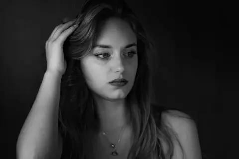 Portret młodej kobiety w odcieniach **black color**. Jej dłoń spoczywa na włosach, a wzrok skierowany jest w bok, w głąb mroku.