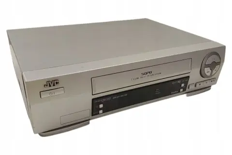 Srebrny vcr JVC z napisem SQPB. Urządzenie posiada przyciski sterujące i slot na kasetę.