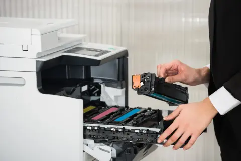 Osoba w czarnym garniturze wymienia toner w drukarce laserowej. Czy drukarka laserowa ma tusz? Nie, używa proszku.