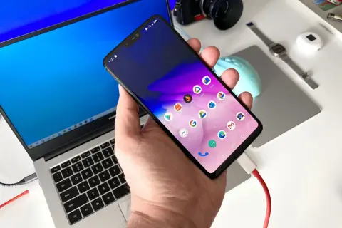 Podłączanie telefonu do laptopa, aby przesłać zdjęcia. Widoczny ekran telefonu z ikonami aplikacji i podłączony kabel USB.