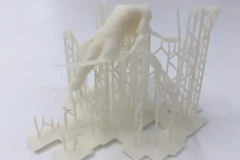 Biały, drukowany w 3D model postaci ludzkiej, przypominający fragment rzeźby lub projektu, osadzony na skomplikowanej, kratownicowej konstrukcji. Format pliku .fbx.