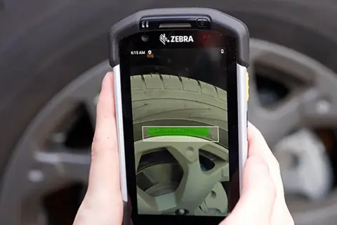 Ręka trzyma urządzenie Zebra, które skanuje oponę. Na ekranie widać tekst "DOT POZO". To pokazuje, jak działa ocr.