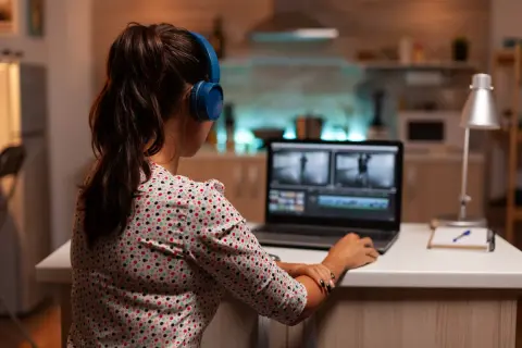 Kobieta w słuchawkach pracuje na laptopie, edytując film. Uczy się, jak zmniejszyć rozmiar filmu, by był łatwiejszy do udostępnienia.
