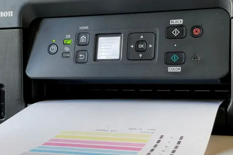 Drukarka Canon wyświetla komunikat "Do którego deseniu jest najbardziej podobny Twój zadrukowany?". Papier z kolorowymi paskami jest częściowo wysunięty.