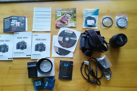 Zestaw akcesoriów do aparatu Canon EOS 1200D: aparat, obiektyw, ładowarka, filtry, instrukcje i płyty DVD.