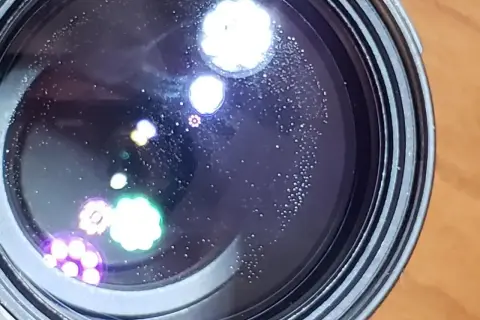Widoczne na soczewce drobne kropki i kolorowe refleksy, przypominające aberrację chromatyczną, tworzą na czarnym tle ciekawe wzory.