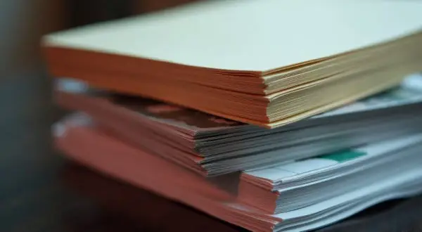 Stos papierów o różnej gramaturze, od jasnego kremowego po różowy, leży na drewnianym blacie.