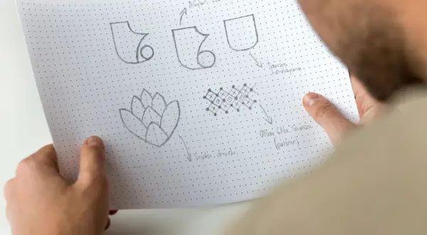 Szkice symboli i wzorów, w tym potencjalny sigil, na papierze w kropki.