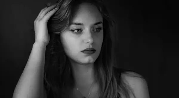 Portret młodej kobiety w odcieniach **black color**. Jej dłoń spoczywa na włosach, a wzrok skierowany jest w bok, w głąb mroku.
