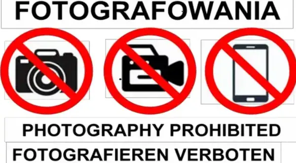 Tablica informuje o zakazie fotografowania. Widoczne są symbole aparatu, kamery i telefonu komórkowego przekreślone czerwoną linią.