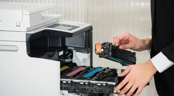Osoba w czarnym garniturze wymienia toner w drukarce laserowej. Czy drukarka laserowa ma tusz? Nie, używa proszku.