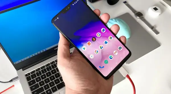 Podłączanie telefonu do laptopa, aby przesłać zdjęcia. Widoczny ekran telefonu z ikonami aplikacji i podłączony kabel USB.