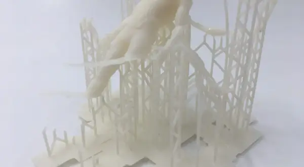 Biały, drukowany w 3D model postaci ludzkiej, przypominający fragment rzeźby lub projektu, osadzony na skomplikowanej, kratownicowej konstrukcji. Format pliku .fbx.