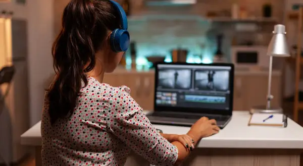 Kobieta w słuchawkach pracuje na laptopie, edytując film. Uczy się, jak zmniejszyć rozmiar filmu, by był łatwiejszy do udostępnienia.