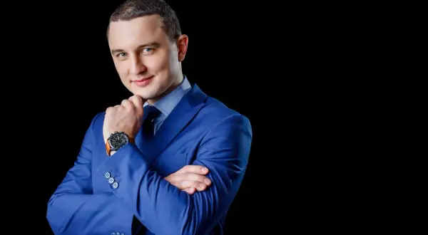Elegancki mężczyzna w niebieskiej marynarce, z dłonią na podbródku. Profesjonalne zdjęcie do CV.