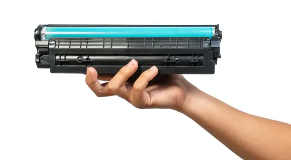 Dłoń trzymająca toner do drukarki HP. Dowiedz się, jak wymienić tusz w drukarce HP, aby drukować bez problemów.