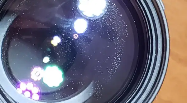 Widoczne na soczewce drobne kropki i kolorowe refleksy, przypominające aberrację chromatyczną, tworzą na czarnym tle ciekawe wzory.