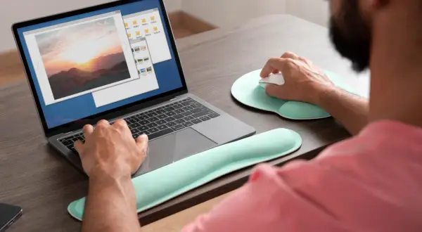 Mężczyzna pracuje na laptopie, przeglądając zdjęcia. Może szukać sposobu, **jak wyostrzyć zdjęcie**, aby poprawić jakość krajobrazu o zachodzie słońca.