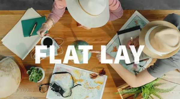 Widok z góry na stół z mapami, globusem, aparatem i notatkami. Dwie osoby planują podróż. To idealny **flat lay** do inspiracji.