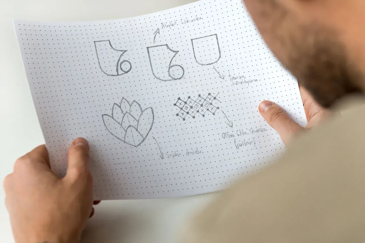 Szkice symboli i wzorów, w tym potencjalny sigil, na papierze w kropki.
