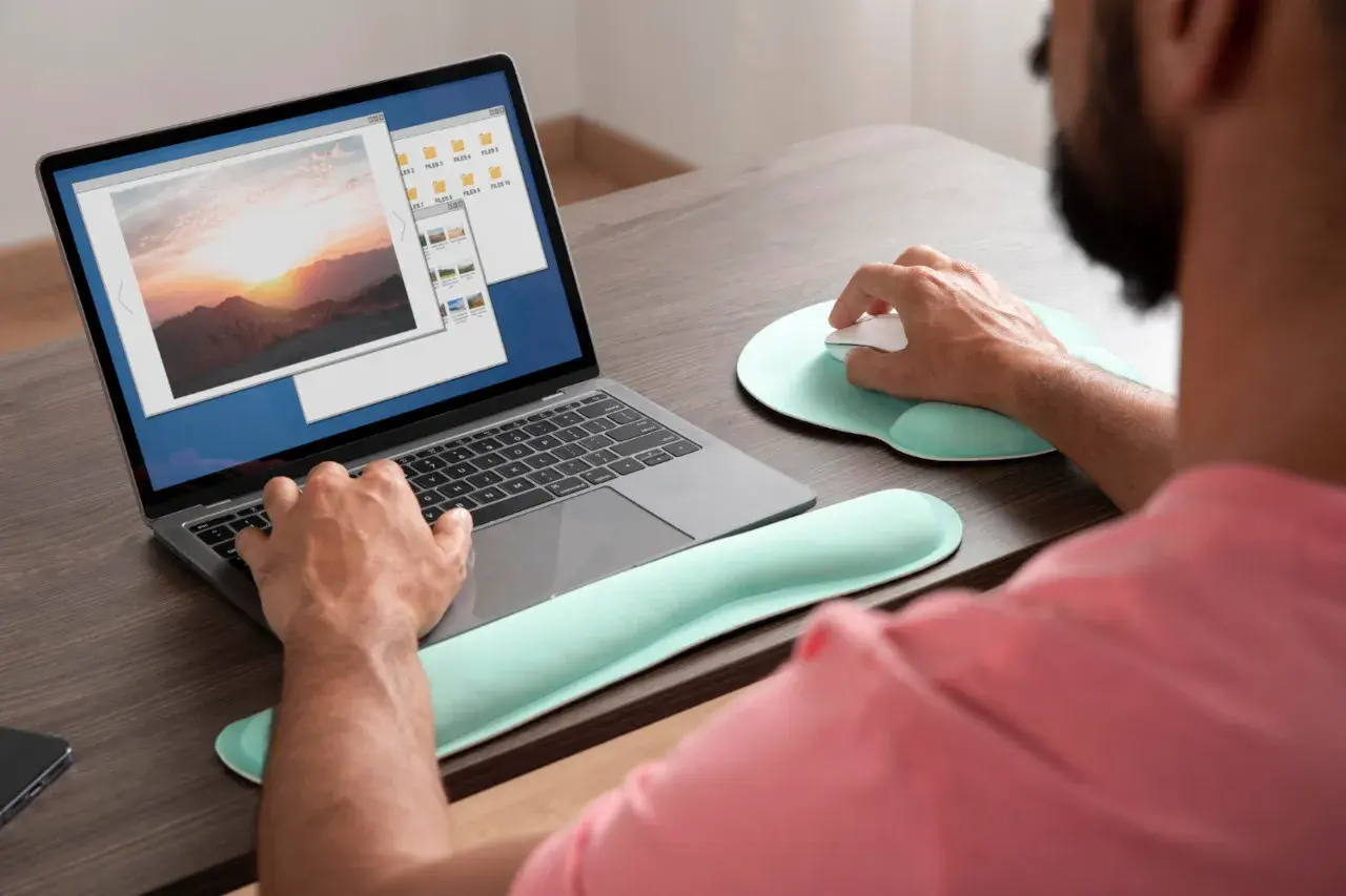 Mężczyzna pracuje na laptopie, przeglądając zdjęcia. Może szukać sposobu, **jak wyostrzyć zdjęcie**, aby poprawić jakość krajobrazu o zachodzie słońca.