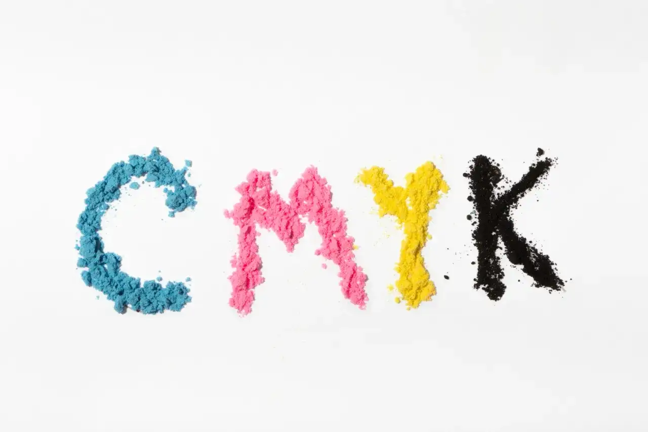Litery CMYK uformowane z proszków: cyjan kolor, magenta, żółty i czarny.