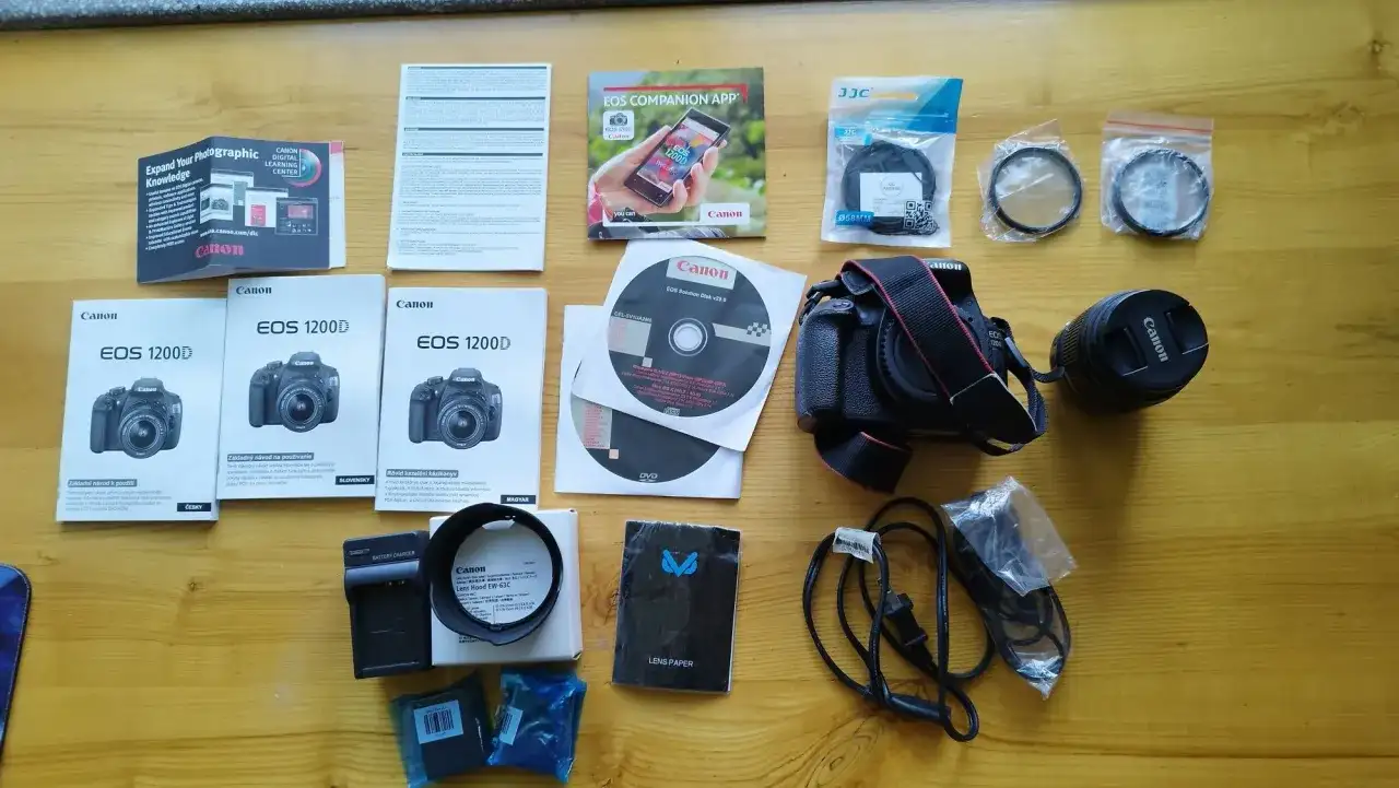 Zestaw akcesoriów do aparatu Canon EOS 1200D: aparat, obiektyw, ładowarka, filtry, instrukcje i płyty DVD.