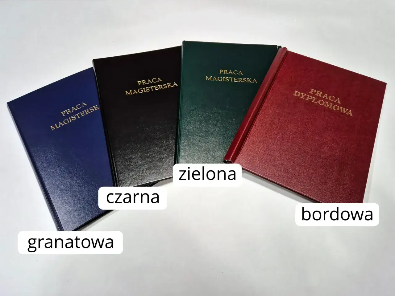 Granatowa, czarna, zielona i bordowa praca magisterska lub dyplomowa, każda w innym kolorze, jakby przygotowana na specjalne paspartu.