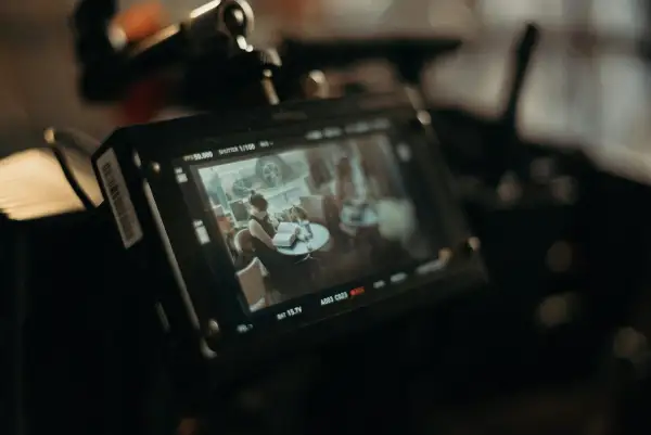 Ekran monitora kamery filmowej pokazuje scenę z kobietą czytającą książkę przy stoliku. To ujęcie z planu filmowego.