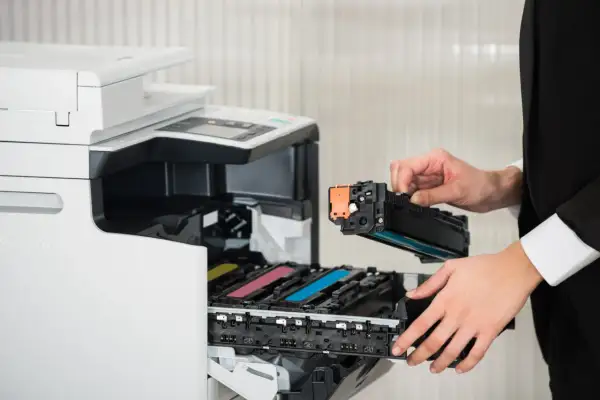 Osoba w czarnym garniturze wymienia toner w drukarce laserowej. Czy drukarka laserowa ma tusz? Nie, używa proszku.
