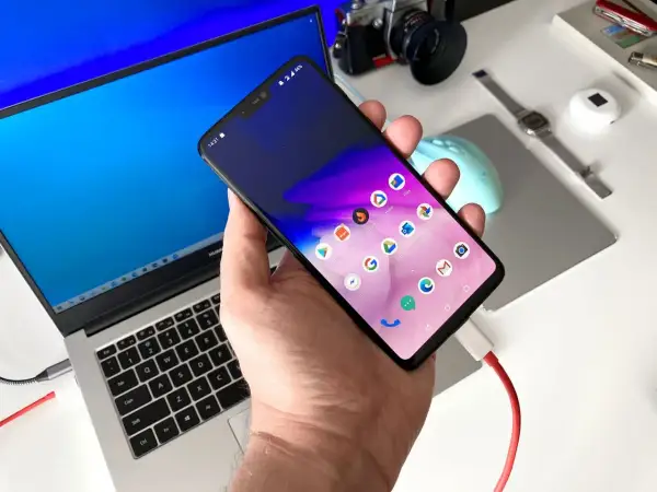 Podłączanie telefonu do laptopa, aby przesłać zdjęcia. Widoczny ekran telefonu z ikonami aplikacji i podłączony kabel USB.