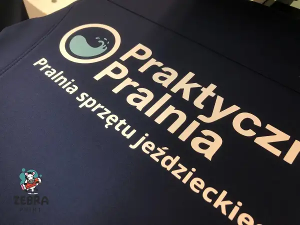 Druk termotransferowy na granatowej odzieży: logo pralni "Praktyczna Pralnia" i napis "Pralnia sprzętu jeździeckiego".