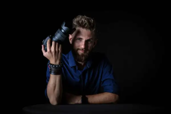 Mężczyzna z aparatem, gotowy do nauki na kursie fotografii.