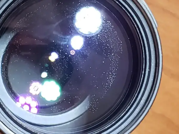 Widoczne na soczewce drobne kropki i kolorowe refleksy, przypominające aberrację chromatyczną, tworzą na czarnym tle ciekawe wzory.