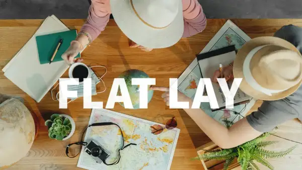Widok z góry na stół z mapami, globusem, aparatem i notatkami. Dwie osoby planują podróż. To idealny **flat lay** do inspiracji.